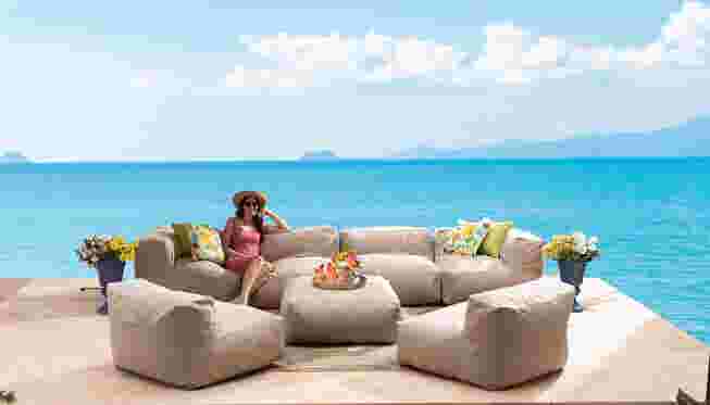 Beige modular seating on a patio overlooking the ocean with a woman sitting on a chair.