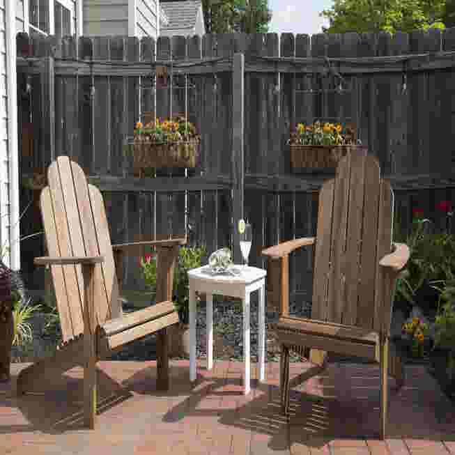 Two wooden Adirondack chairs with a small table on a patio.