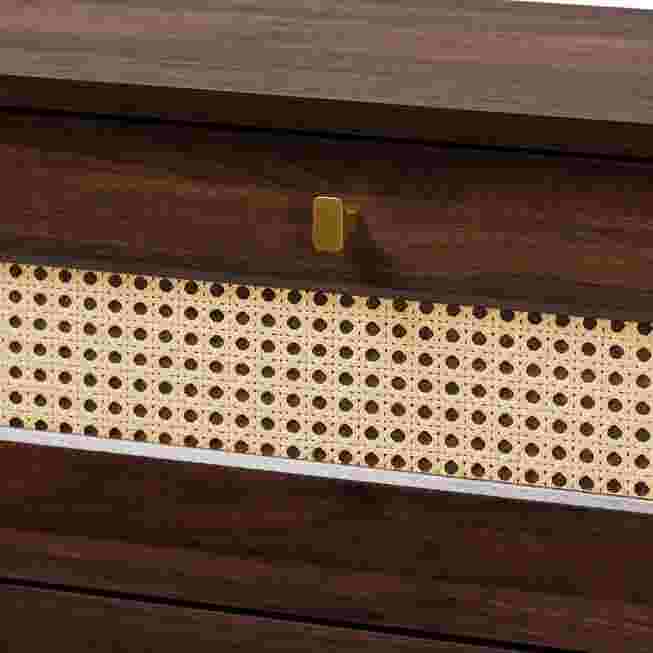 A close-up of the rattan drawer front and the handle of a dark wood chest.