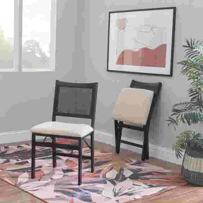 Two black folding chairs with light-colored cushions, one folded, in a room with a patterned rug.