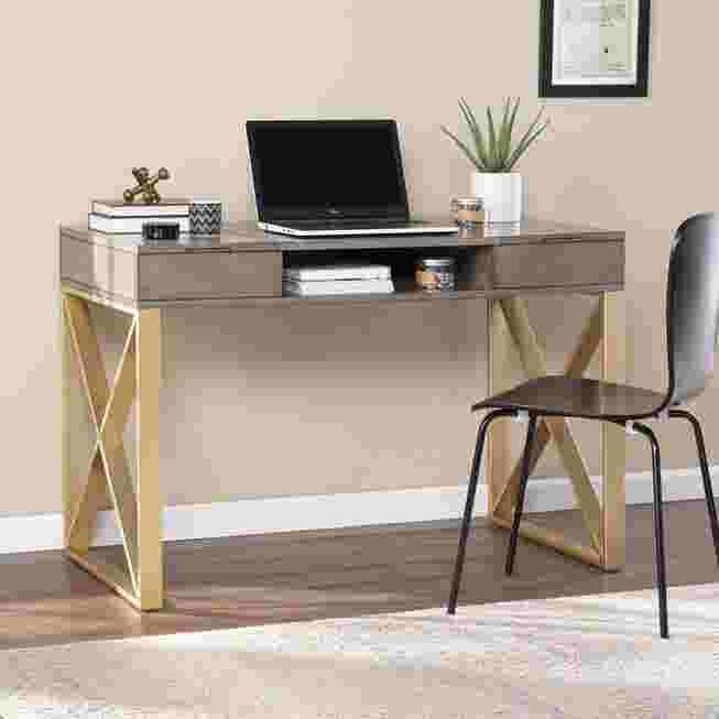 A modern desk with a gray top and gold X-shaped legs, featuring a laptop and books on the surface.