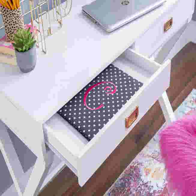 Open drawer of a white writing desk showing a polka dot mat with a pink monogram