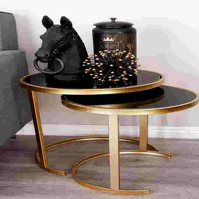 Two gold metal accent tables with black tops used as a side table with decorative items.