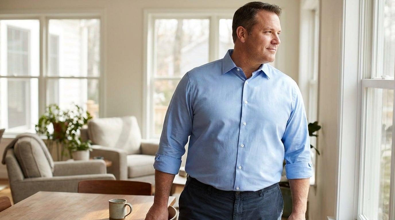 Big and tall man wearing a fitted button-down shirt with sleeves rolled, standing in natural light