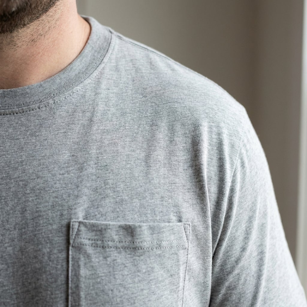 Close-up of a taped crewneck seam and chest pocket stitching on a lightweight pocket tee
