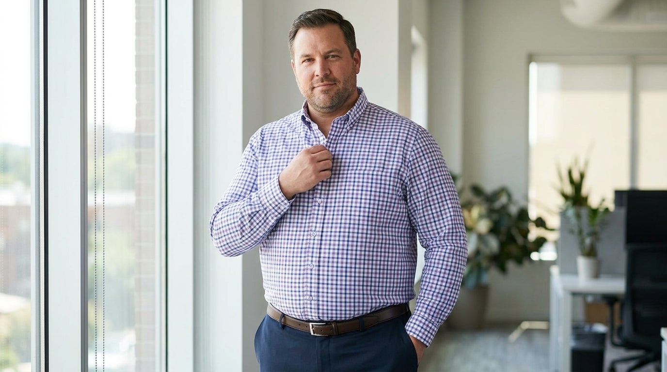 Big & Tall man in a wrinkle-free dress shirt adjusting his collar in a bright office