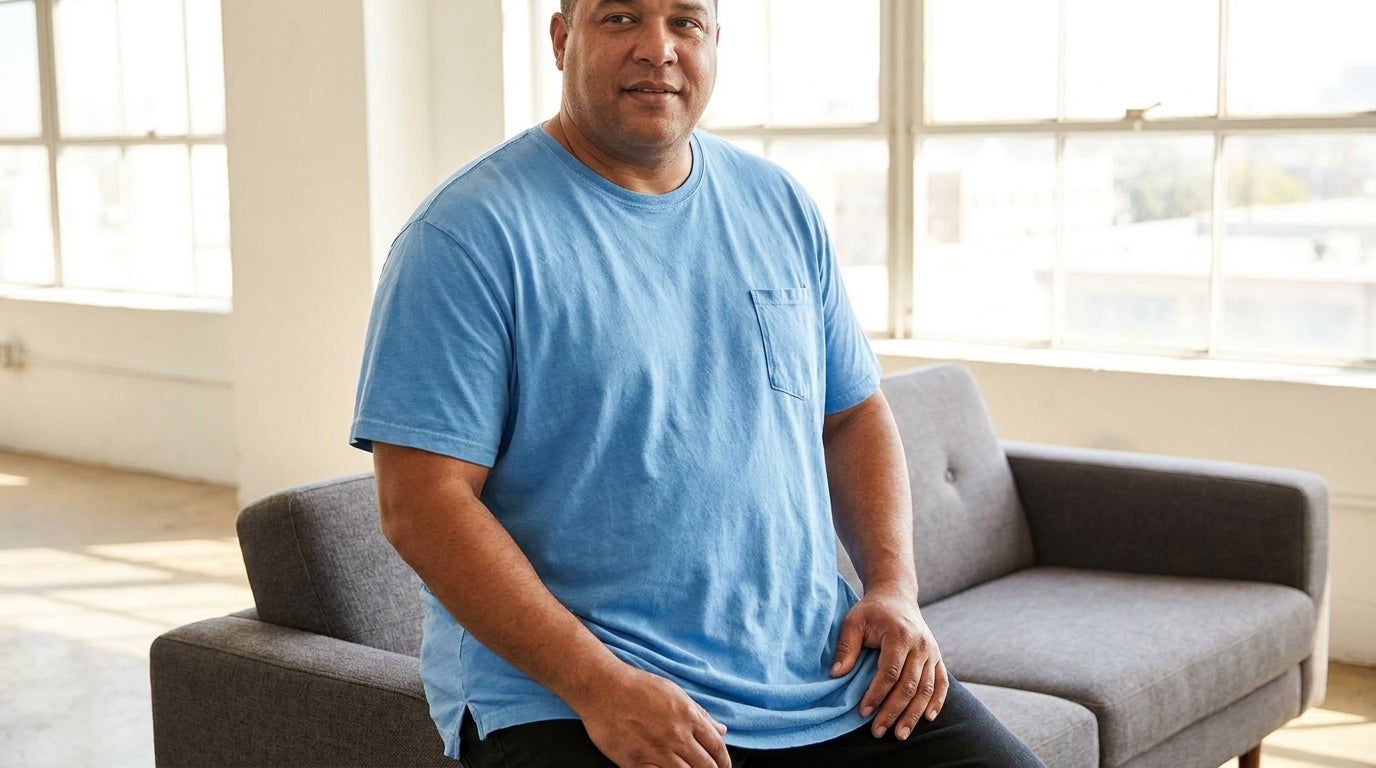 Big and tall man in a heather gray longer-length crewneck pocket tee relaxing in a bright loft